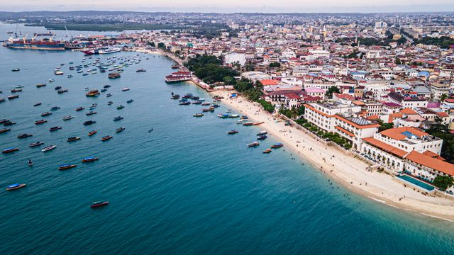 Vista aérea de la costa de Zanzíbar con barcos, playas, edificios históricos y aguas turquesas del océano Índico.