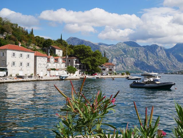 Pueblo costero a orillas de la bahía de Kotor, en Montenegro, con casas de piedra, embarcaciones y montañas al fondo.