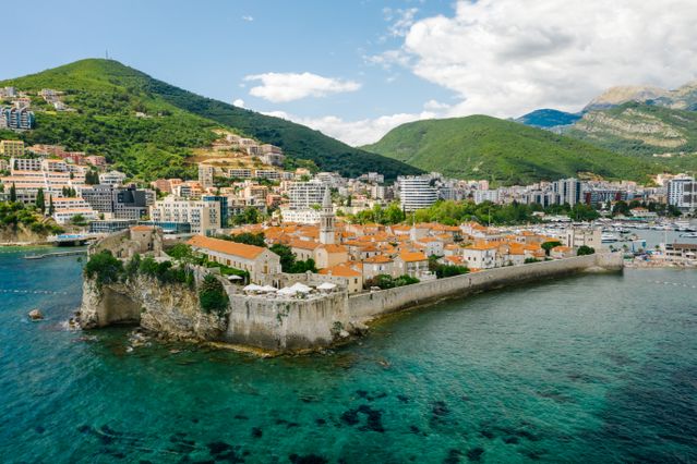 Vista aérea del casco antiguo amurallado de Budva, Montenegro, rodeado por las aguas del mar Adriático y montañas verdes.