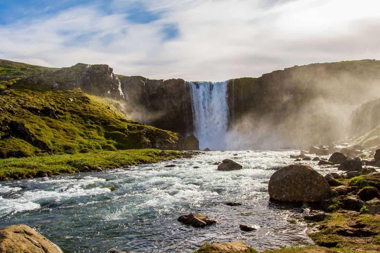 Cascada rodeada de campos verdes y un río en Islandia durante los meses de clima más templado.