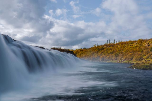 Cascada rodeada de vegetación otoñal en Islandia durante un recorrido por sus paisajes naturales.