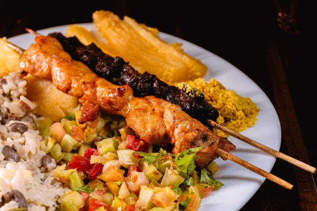 Churrasco brasileño con farofa y acompañamientos tradicionales Brochetas de carne asada al estilo brasileño acompañadas con farofa, vinagreta, arroz con frijoles y mandioca.