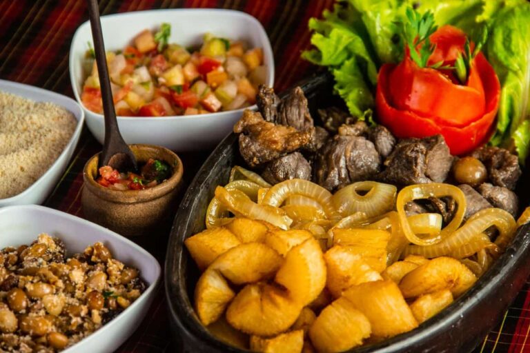 Plato de comida brasile&ntilde;a con carne, mandioca frita, cebolla, farofa, frijoles, ensalada y vinagreta.