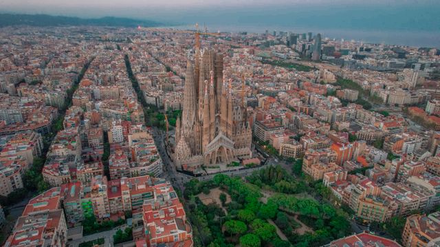 Cómo moverse por Barcelona en metro, bus y tren Vista aérea de Barcelona con la Sagrada Familia y el trazado urbano de la ciudad hasta el mar Mediterráneo.