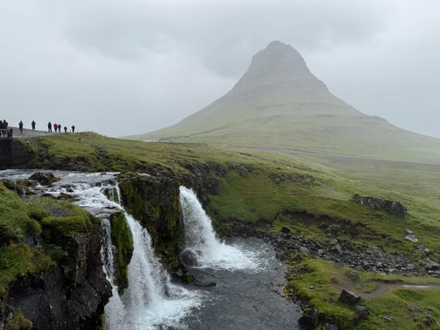 Monte Kirkjufell y cascada Kirkjufellsfoss en la península de Snæfellsnes, Islandia, bajo un cielo nublado.
