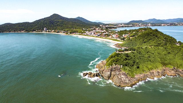 Costa de Brasil en verano: enero o febrero de 2027 Vista aérea de una playa de Brasil rodeada de colinas verdes y una localidad costera