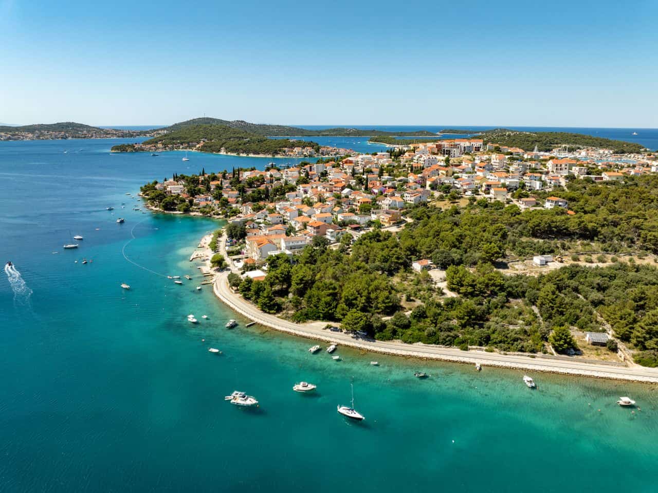 Vista aérea de una localidad costera de Croacia rodeada de aguas turquesas, pequeñas islas y embarcaciones en el mar Adriático.