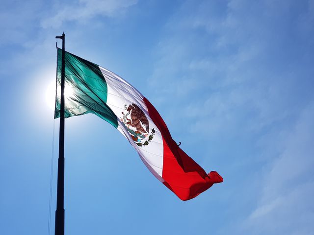 Bandera de México ondeando bajo un cielo despejado, símbolo de los destinos familiares para viajar por el país.