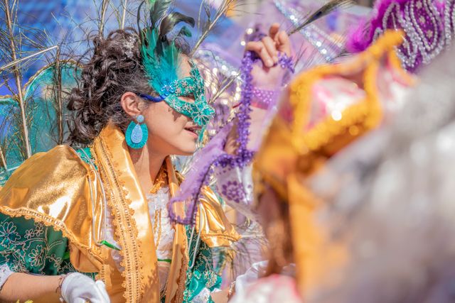 Participante con máscara, plumas y traje dorado y verde durante un desfile de Mardi Gras.