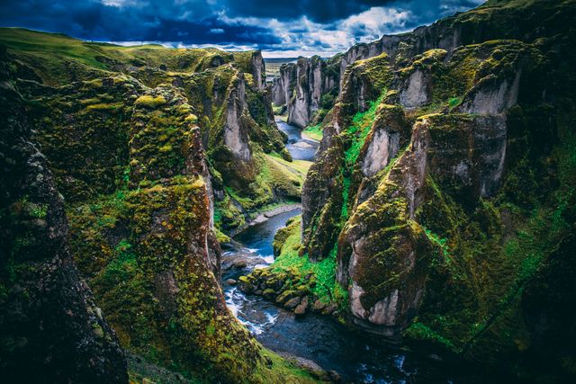Cañón Fjaðrárgljúfur en Islandia, con paredes rocosas cubiertas de musgo y un río entre el paisaje verde.