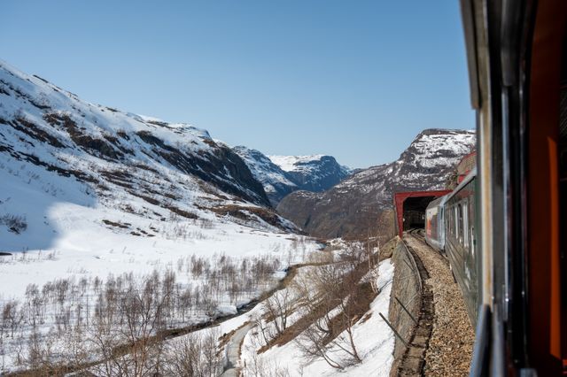Tren de la Flåmsbana recorriendo un paisaje nevado entre montañas en Noruega.