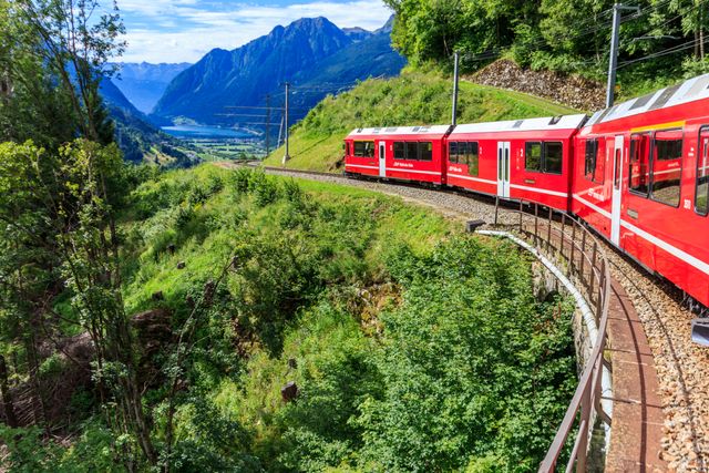 Tren rojo del Glacier Express recorriendo un paisaje alpino verde en Suiza, con montañas al fondo.