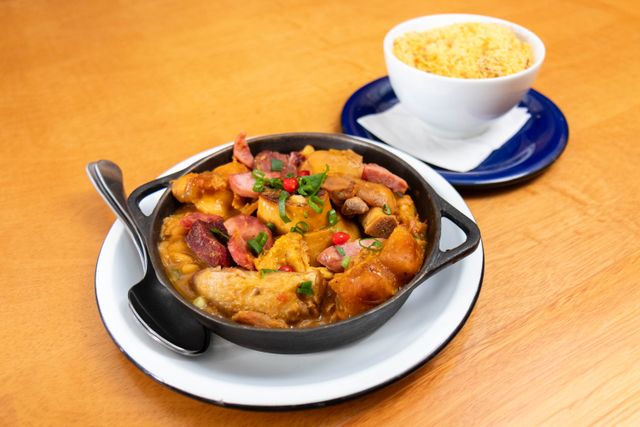 Guisos y platos tradicionales de la gastronomía brasileña Guiso brasileño con distintas carnes, salchicha, frijoles y verduras, acompañado con farofa.