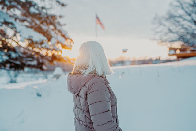 Invierno en Estados Unidos 2026-2027 y destinos con nieve Viajera con abrigo en un paisaje nevado de Estados Unidos durante el invierno, con una bandera estadounidense al fondo.