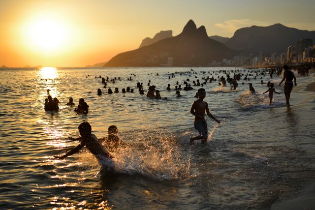 Playa de Ipanema al atardecer en Río de Janeiro con niños Niños y familias bañándose en la playa de Ipanema al atardecer, con el Morro Dois Irmãos al fondo en Río de Janeiro.