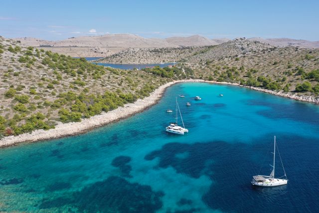 Navegar por las islas de Croacia en el mar Adriático Veleros fondeados en una bahía de aguas turquesas entre islas rocosas de la costa de Croacia.