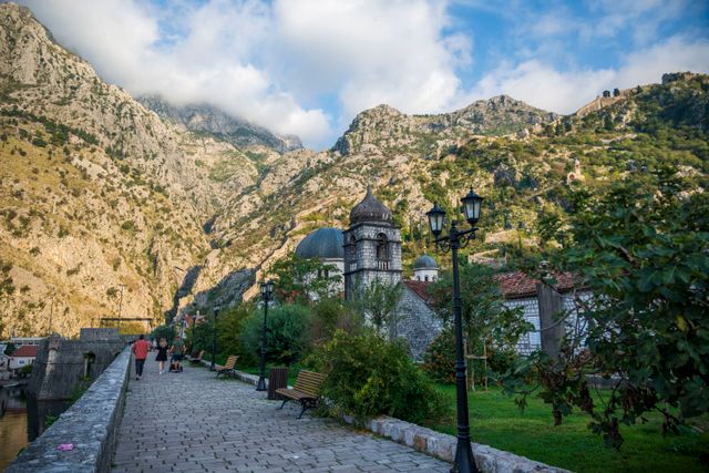 Vista del casco histórico de Kotor, en Montenegro, con una iglesia de piedra, paseo junto a la muralla y montañas al fondo.