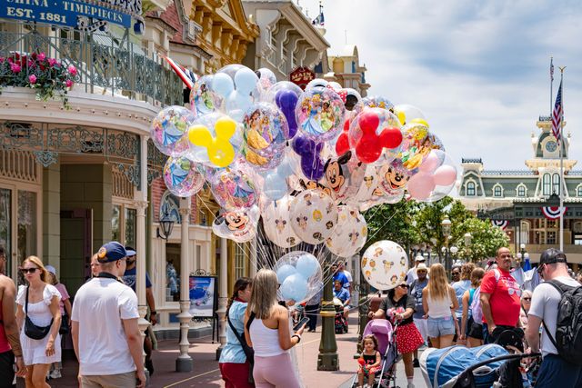 Main Street U.S.A. en Magic Kingdom con numerosos visitantes y globos de personajes de Disney durante un día concurrido.