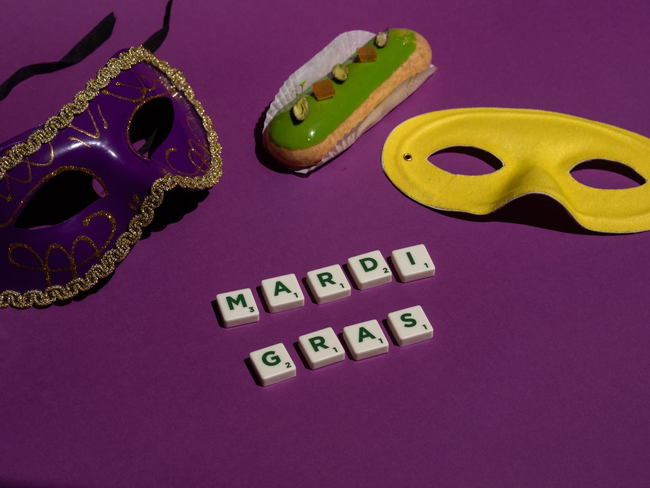Máscaras de carnaval, letras con la frase Mardi Gras y un dulce decorado sobre un fondo morado.