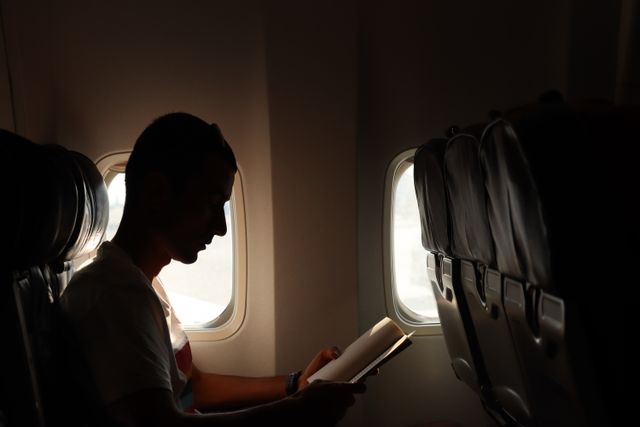 Viajar en avión con o sin WiFi a bordo Pasajero leyendo junto a la ventanilla durante un vuelo comercial