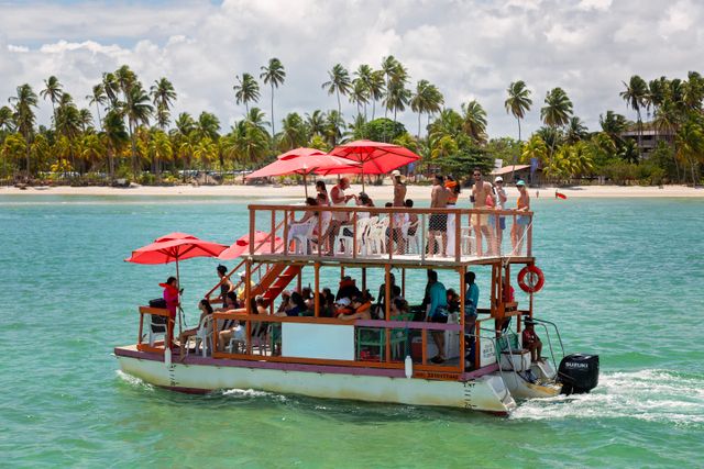 Turistas en una embarcación frente a una playa de Porto de Galinhas, Pernambuco, rodeada de aguas turquesas y palmeras.