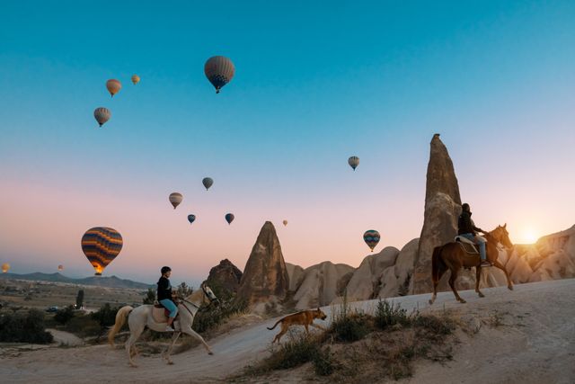 Paseo a caballo y globos sobre Capadocia al amanecer Viajeros a caballo entre chimeneas de hadas mientras vuelan globos aerostáticos sobre Capadocia, Turquía.