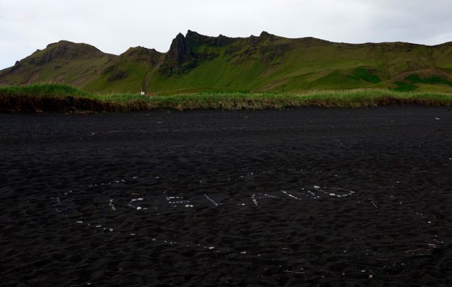 Playa de arena negra rodeada de montañas verdes en Islandia durante los meses de clima más templado.