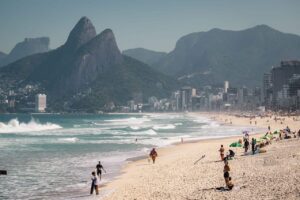Playa de Ipanema en R&iacute;o de Janeiro con familias y ba&ntilde;istas, y el Morro Dois Irm&atilde;os al fondo.