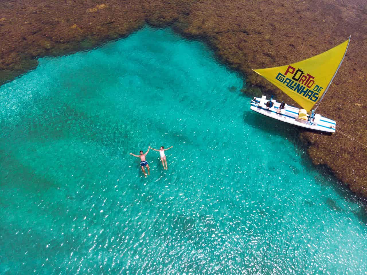 Vista aérea de una piscina natural en Porto de Galinhas, Pernambuco, con aguas turquesas y una jangada tradicional.