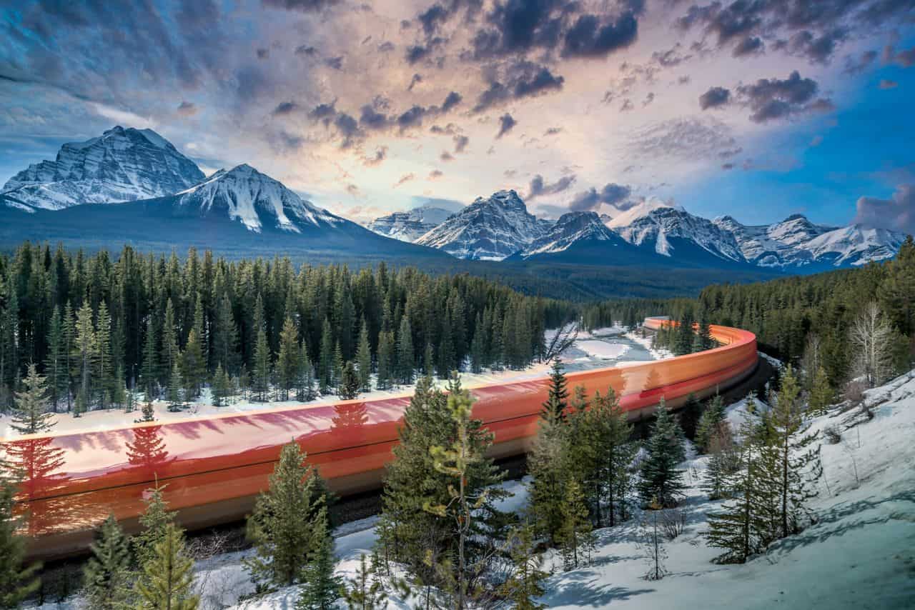 Tren recorriendo las Montañas Rocosas de Canadá entre bosques y cumbres nevadas durante el invierno.