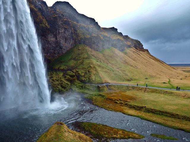 Cascada Seljalandsfoss en el sur de Islandia, rodeada de montañas y senderos bajo un cielo nublado.