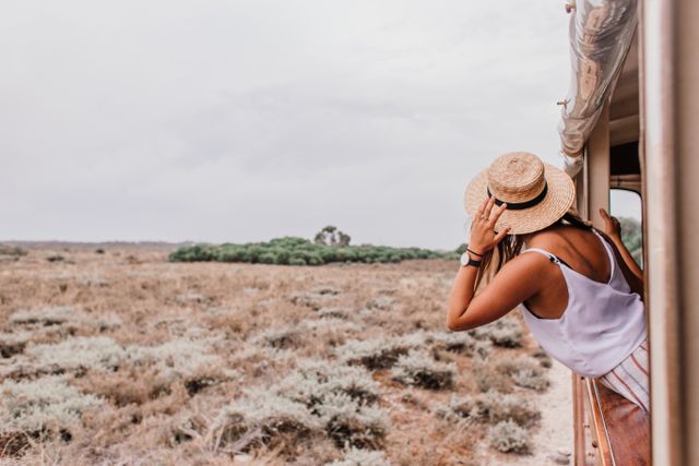 Viajera asomada a la ventana de un tren en una zona árida del interior de Australia durante el recorrido de The Ghan.