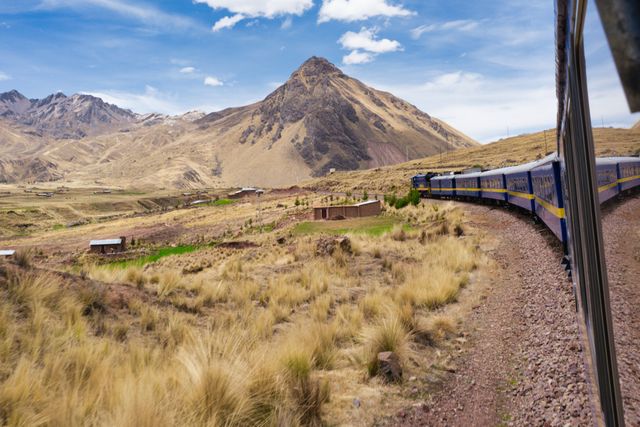Tren turístico recorriendo un paisaje de alta montaña en los Andes de Perú, entre valles y cumbres escarpadas.