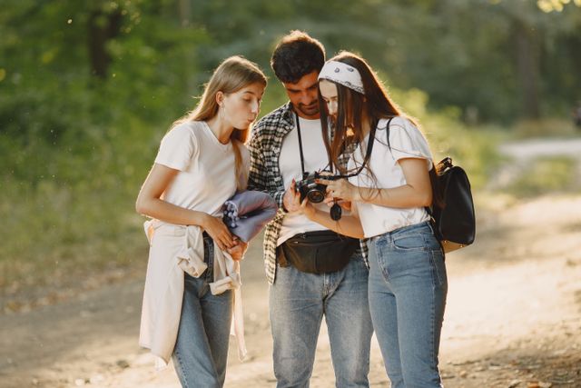 Tres jóvenes viajeros revisan fotografías en una cámara durante un recorrido al aire libre.