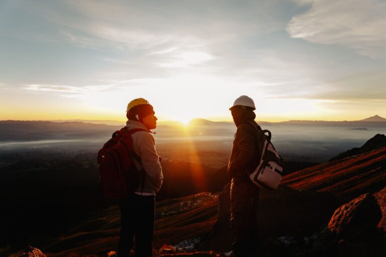 Dos viajeros con mochilas contemplando el amanecer desde una zona de monta&ntilde;a