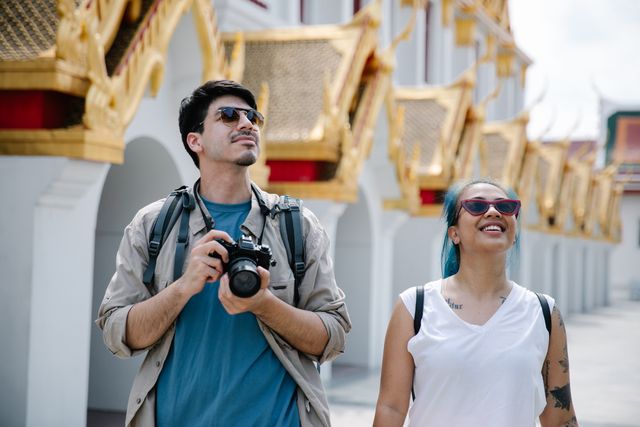Dos viajeros observan un templo de arquitectura asiática mientras recorren un destino extranjero.