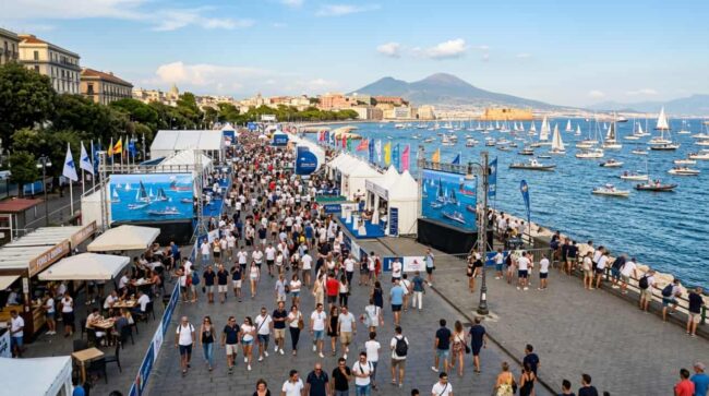 Público junto al paseo marítimo de Nápoles durante un evento náutico con veleros y el Vesubio al fondo