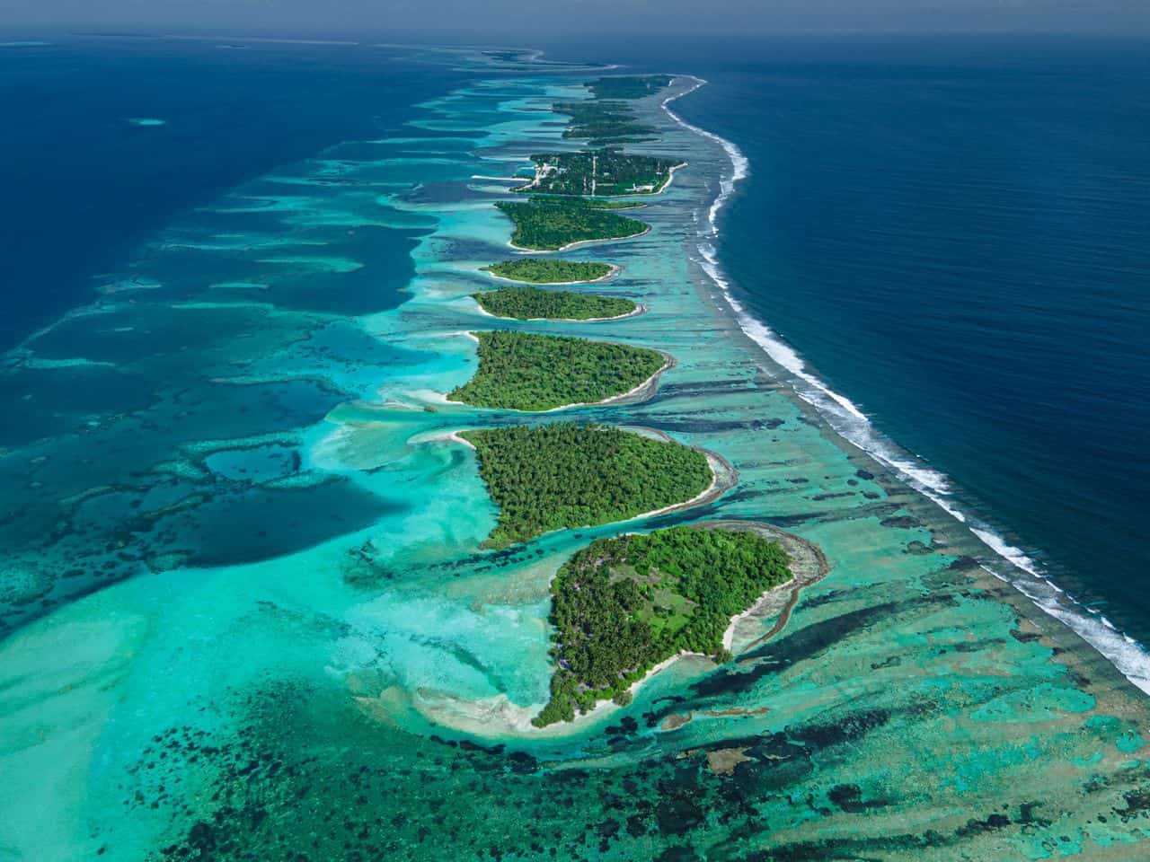 Vista aérea de una cadena de pequeñas islas tropicales rodeadas de arrecifes y aguas turquesas