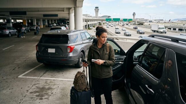 Viajera recoge un auto alquilado en un aeropuerto de Estados Unidos y revisa en su teléfono las condiciones del viaje