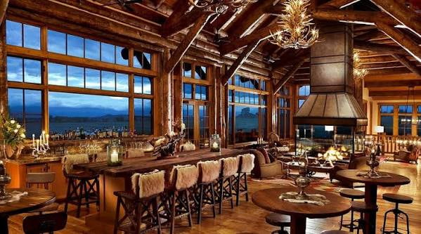 Interior de Brush Creek Ranch en Wyoming con decoración rústica, chimenea y grandes ventanales hacia el paisaje