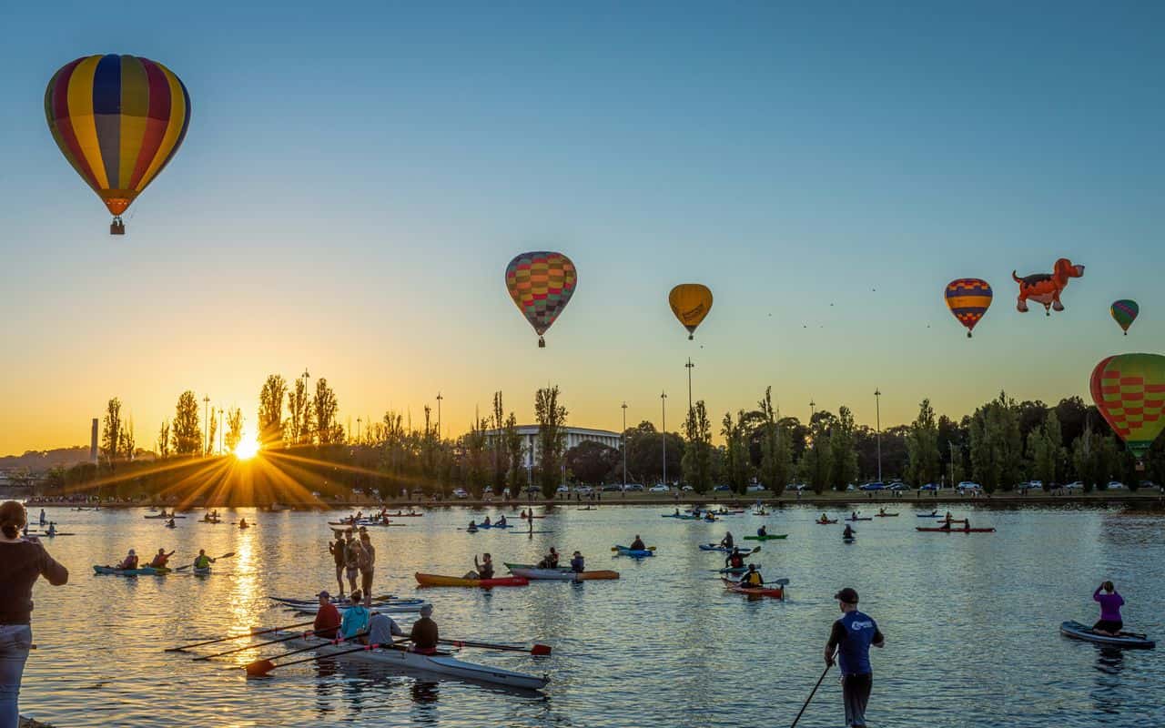 Globos aerostáticos sobre el lago Burley Griffin en Canberra al amanecer, con personas practicando kayak