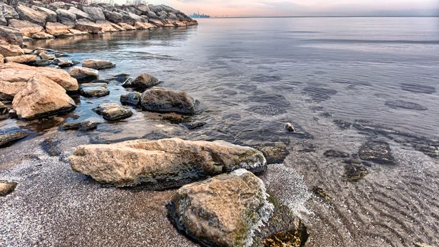 Costa rocosa del lago Ontario con aguas tranquilas y piedras junto a la orilla.