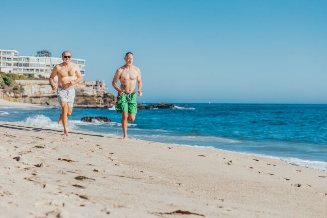 Dos hombres corren por la playa junto al mar en una ciudad costera