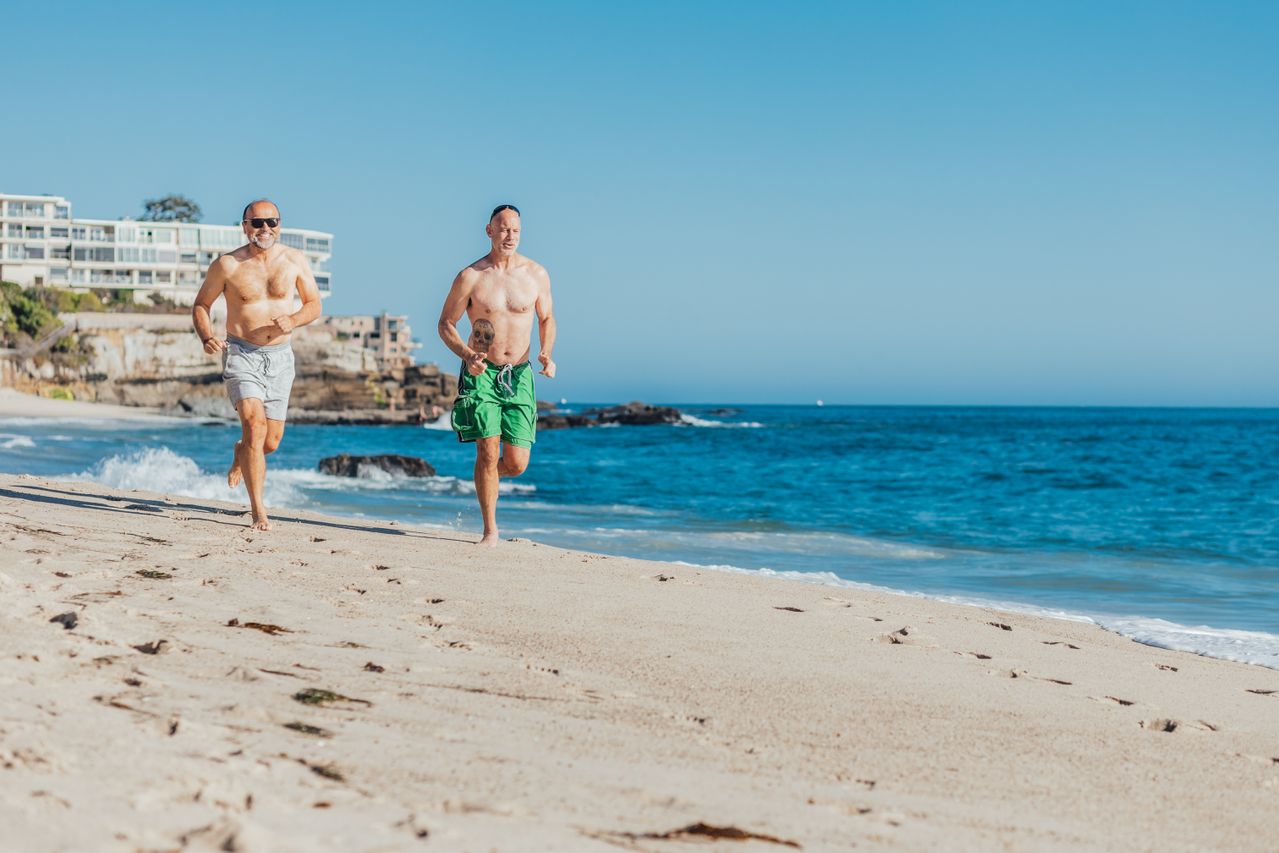 Dos hombres corren por la playa junto al mar en una ciudad costera