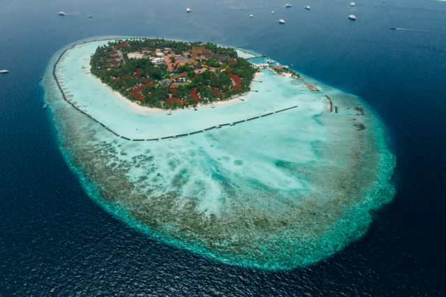 Maldivas: clima y mejor época para viajar Vista aérea de una isla de Maldivas rodeada por una laguna turquesa y arrecifes