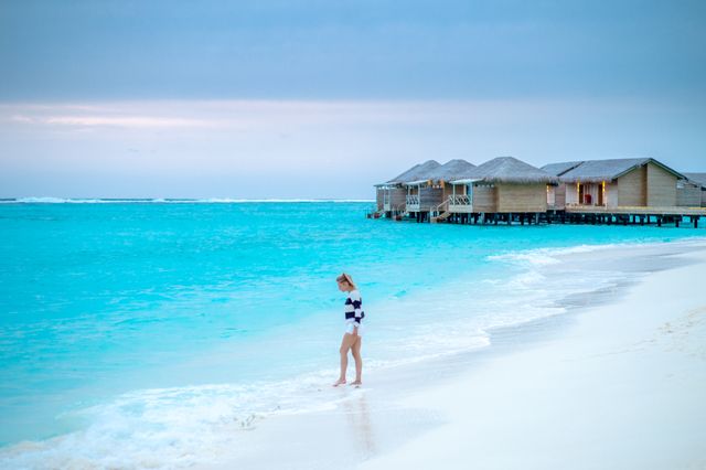 Mejor época para viajar a Maldivas y disfrutar de sus playas Viajera camina por una playa de Maldivas con villas sobre el agua y mar turquesa
