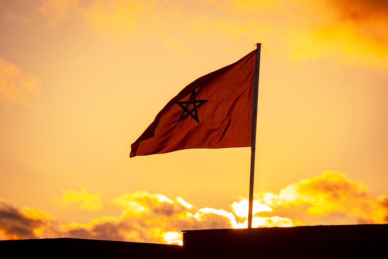 Bandera de Marruecos ondeando al atardecer bajo un cielo naranja