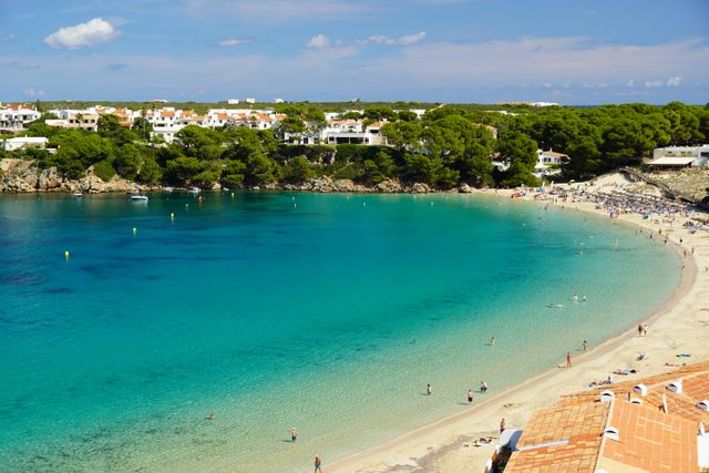 Playa de aguas turquesas rodeada de pinares y casas blancas en Menorca, Islas Baleares