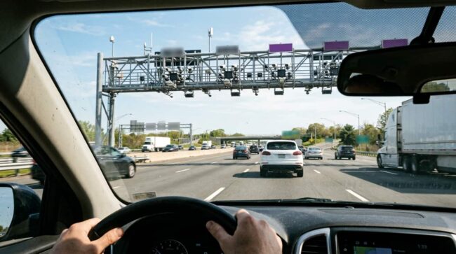 Conductor pasa con un auto por un pórtico de peaje electrónico en una autopista de Estados Unidos