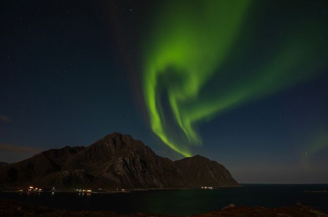 Aurora boreal verde sobre montañas y costa durante una noche despejada